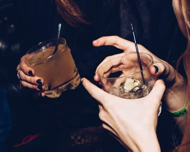 Two people holding cocktails with straws, one with a wristband, emphasizing night out drink safety.