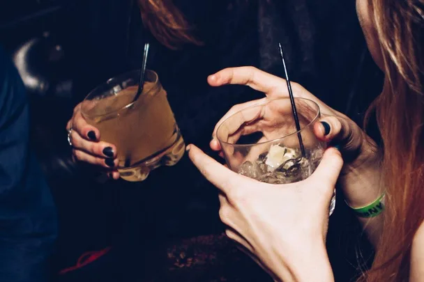 Two people holding cocktails with straws, one with a wristband, emphasizing night out drink safety.