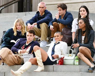 A group of well-dressed young adults sitting on outdoor steps, depicting characters from "Gossip Girl" reboot, looking relaxed.