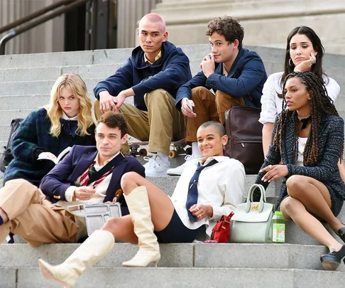 A group of well-dressed young adults sitting on outdoor steps, depicting characters from "Gossip Girl" reboot, looking relaxed.