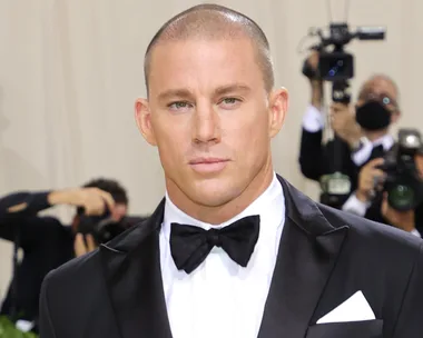 A man in a black tuxedo with a bow tie stands in front of photographers.