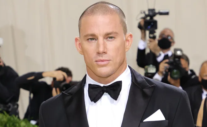 A man in a black tuxedo with a bow tie stands in front of photographers.