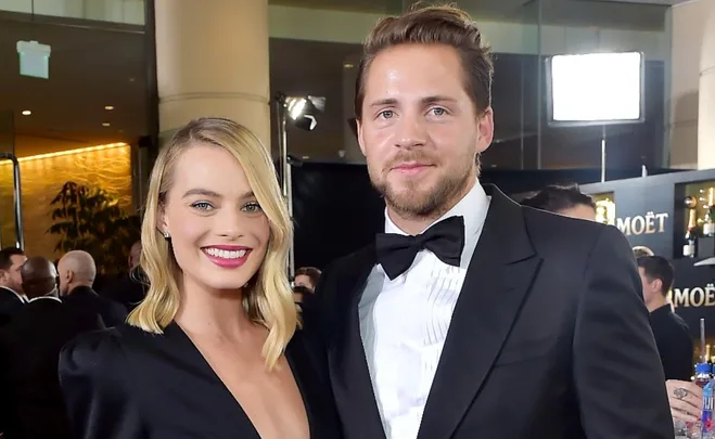 A couple dressed formally at an event, with Moët branding and crowd in the background.