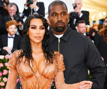 Kim Kardashian and Kanye West pose at a glamorous event, with Kim in a stylish dress and Kanye in a jacket.