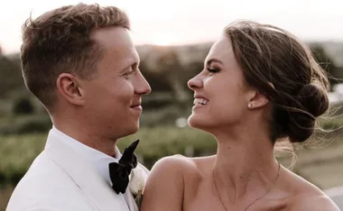 A couple smiling at each other outdoors during their wedding, with a sunset in the background.