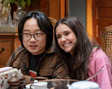 Two characters from "Love Hard" sit at a dining table, smiling warmly.