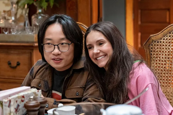 Two characters from "Love Hard" sit at a dining table, smiling warmly.