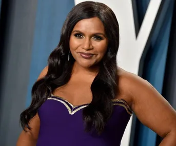 A woman in a purple dress poses on the red carpet with a soft smile.