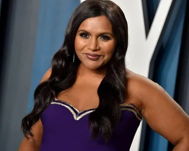 A woman in a purple dress poses on the red carpet with a soft smile.