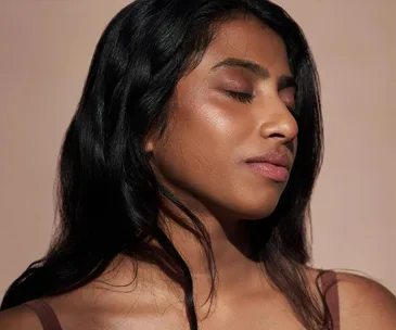 A woman with closed eyes and smooth skin, showcasing sustainable makeup against a neutral background.