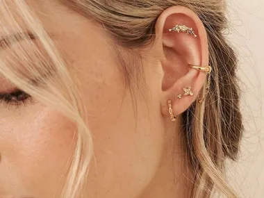 Close-up of a woman's ear with multiple gold earrings, featuring studs, hoops, and a cuff.