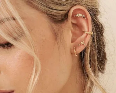 Close-up of a woman's ear with multiple gold earrings, featuring studs, hoops, and a cuff.