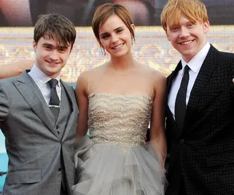 Daniel Radcliffe, Emma Watson, and Rupert Grint smiling at a Harry Potter premiere, dressed in formal attire.