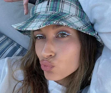 Person in a plaid bucket hat making a duck face selfie, lying on a striped cushion.