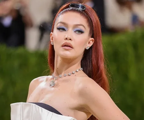 A person with long red hair and elegant dress at a formal event, wearing a sparkling necklace, with a green blurred background.