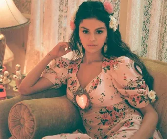 A woman in a floral dress with flowers in her hair, sitting on a couch, with a glowing heart decoration.