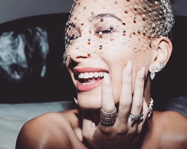 Smiling woman with jeweled veil and stylish tooth gems, adorned with rings and earrings.