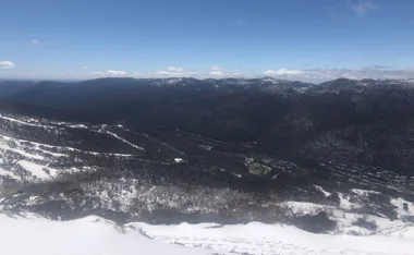 Aerial view of Thredbo, Australia, showcasing snow-covered mountains and a clear blue sky.