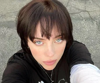 Woman with short, dark hair and blunt bangs looking at camera in a casual outdoor setting.