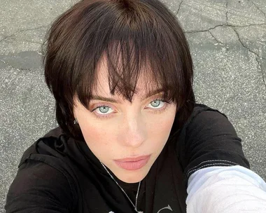 Woman with short, dark hair and blunt bangs looking at camera in a casual outdoor setting.