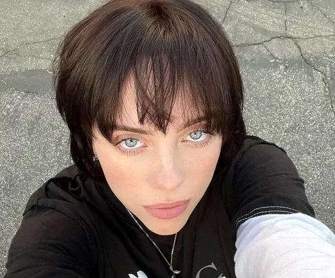 Woman with short, dark hair and blunt bangs looking at camera in a casual outdoor setting.