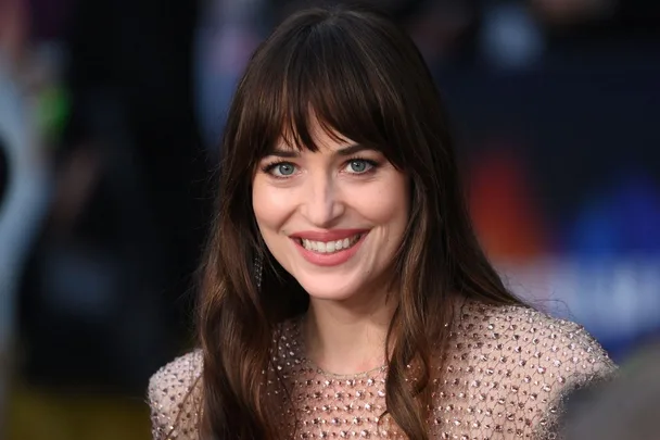 Smiling woman with long brown hair and bangs, wearing a shiny, beaded top.