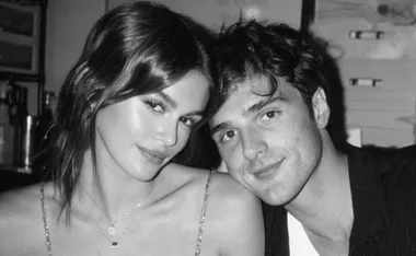 Couple sitting closely together in a black and white photo, smiling softly at the camera.