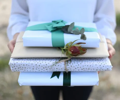 Person holding three wrapped gifts with bows and flowers.