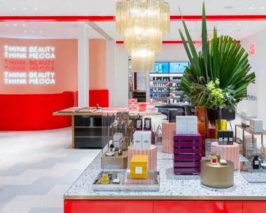 A modern Mecca beauty store interior with vibrant red accents, a chandelier, and perfume displays.