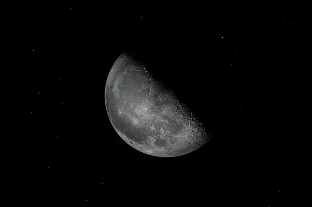 A black and white image of a crescent moon with visible craters set against a starry night sky.