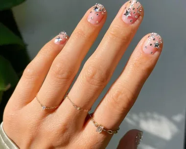 Close-up of a hand with nude nails adorned with silver star and dot embellishments suitable for New Year's Eve.