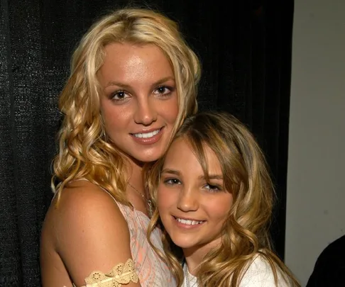 Two women smiling and embracing in front of a black backdrop.