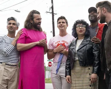 The Queer Eye cast stands with Sarah Lim, who is wearing glasses and a leather jacket, smiling outdoors.