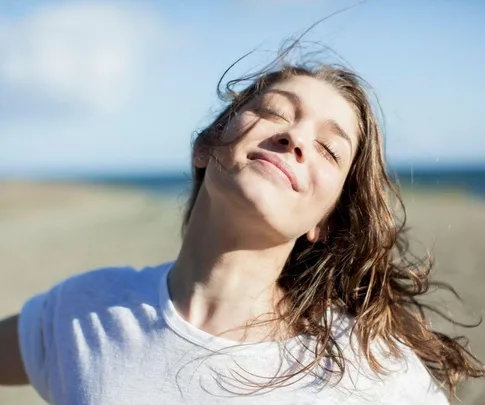 A woman smiling with closed eyes, enjoying the breeze on a sunny day at the beach.