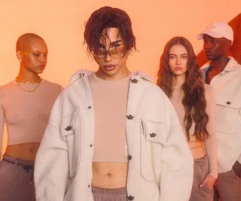 A diverse group models neutral-toned clothing in a stylish, warm-toned setting for the Boys Lie x Ariel Tejada collection.