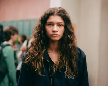 Zendaya as Rue Bennett from Euphoria Season 2, standing in a hallway with a serious expression.