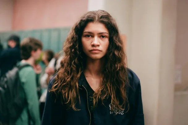 Zendaya as Rue Bennett from Euphoria Season 2, standing in a hallway with a serious expression.