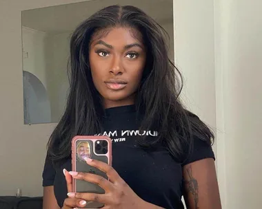 Woman taking a mirror selfie with a phone, wearing a black t-shirt, in a room with neutral walls.