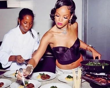 Two women plating food in a kitchen; one in a white coat, the other in a corset top.