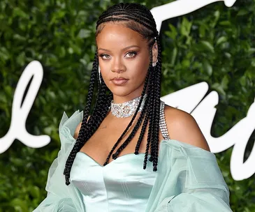 Woman with braided hair in light blue gown and jeweled necklace against a leafy background at a formal event.