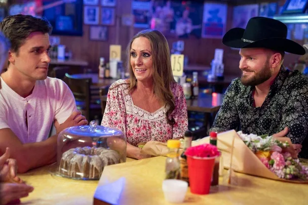 Three people seated at a table in a lively restaurant, chatting with a cake in the center.