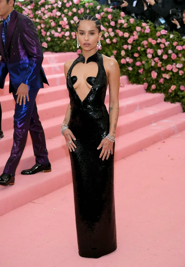 Woman in a black sequin dress on pink carpet with floral background.