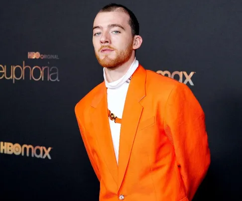 Man in an orange suit at a "Euphoria" event, standing in front of HBO Max branding on a black background.