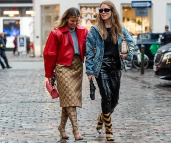 Two stylish women walking on a cobblestone street, one in a red jacket and Gucci print, the other in denim and leather.