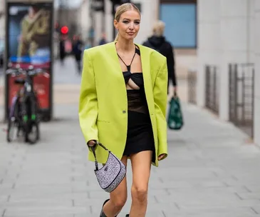 Woman in a lime green blazer and black dress walks on a city street during London Fashion Week 2022.