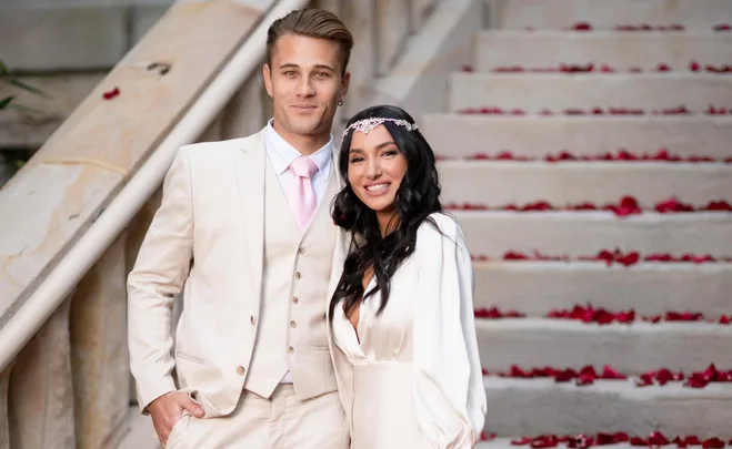 A couple from Married at First Sight Australia 2022 standing on rose-petal-covered steps, smiling.