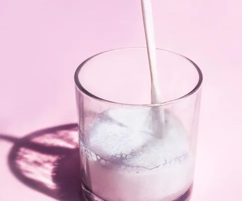 Glass of milk being poured on a pink background.