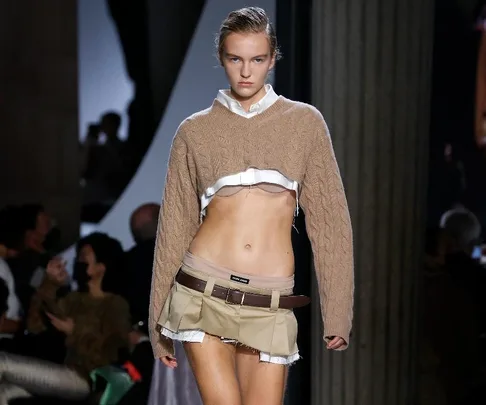 Model in a beige Miu Miu mini skirt and cropped sweater walking a fashion runway.