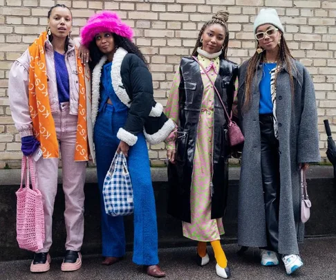 Four stylish individuals at Copenhagen Fashion Week 2022 in vibrant outfits, standing against a brick wall.