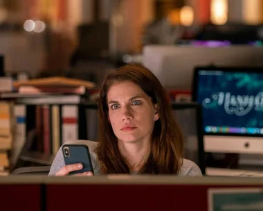 Anna Chlumsky as a journalist in "Inventing Anna," sitting in an office, looking at a smartphone.